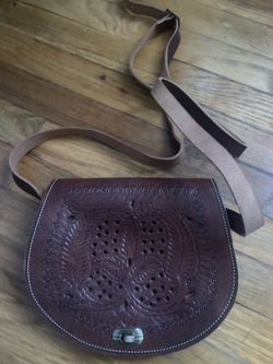 Hand-tooled leather crossbody bag in a deep brown color. This bag has a decorative floral and geometric pattern on the front flap with a metal twist-l
