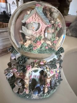 Vintage musical snow globe featuring birds, flowers, and a detailed garden cottage base.