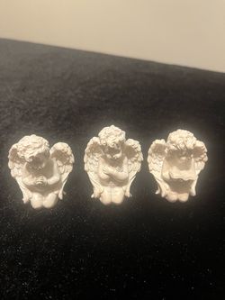 Detailed set of three white resin cherub figurines. Each angel is in a different kneeling pose: one praying, one with arms crossed, and one reading a 