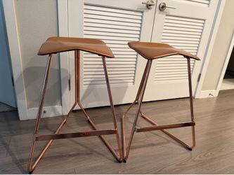 ClassiCon Triton bar stools featuring a copper-plated steel frame and a brown leather seat.