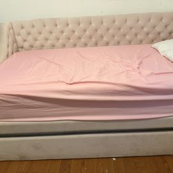 Pink velvet upholstered daybed with a tufted headboard and a pull-out trundle.