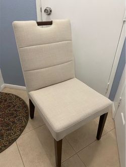 4 Beautiful Beige Fabric Dining Chairs with Walnut Wood Legs and a Small Detail on the Backrest; BRAND NEW.
