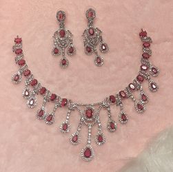 Red Statement American Diamond Necklace Set consists of a silver-plated necklace and matching earrings featuring red cubic zirconia stones. 