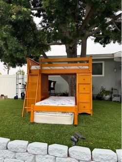 The wooden bunk bed includes both mattresses and features an office desk, five drawers, and a bookshelf.