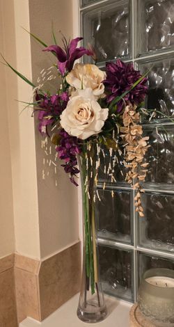 Floral arrangement featuring artificial flowers, such as roses and lilies, arranged in a tall glass