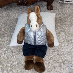 A plush sitting horse toy wearing a silver vest and black bottoms.18”