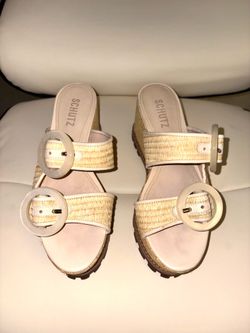 sandalias son el modelo Schutz Bella, caracterizado por su material de rafia natural y hebillas circulares grandes