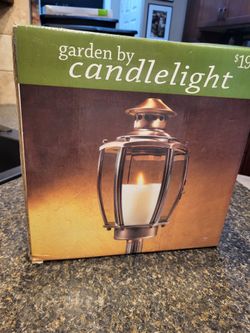 Garden by Candlelight outdoor candle lantern packaged in a box, featuring a classic brass-toned metal frame with glass panels designed to hold a pilla