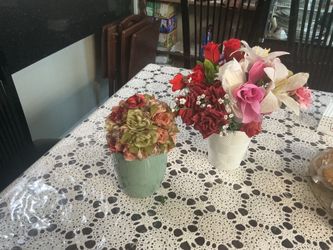 Colorful artificial flower arrangements. Two pieces. One has red, green, and peach flowers in a green vase. Other has red roses, white lilies, pink, a