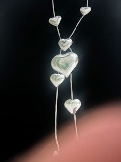 Elegant silver-toned necklace with multiple polished heart pendants. This piece has a thin snake chain and features six hearts of varying sizes. The m