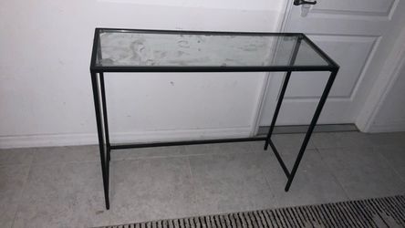 Modern glass-top console table featuring a sleek black metal frame and clear glass surface