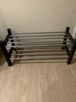 Sturdy two-tier shoe rack with a black wood or composite frame and silver-toned metal rods. This unit has two levels for storage and a minimalist desi