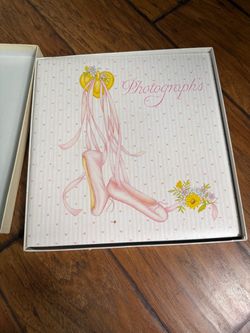 Photographs album with a ballet slipper design, in a matching storage box. Includes the original storage box Features a pink and white heart-patterned