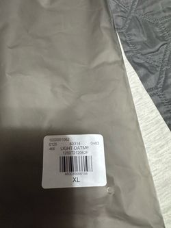 Fear of God ESSENTIALS Light Oatmeal T-Shirt, size XL, with black lettering on the front and back.