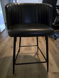 3 black faux-leather counter-height barrel stools with channel stitching and metal legs.