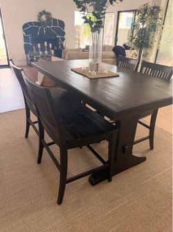rustic dark wood dining set featuring a solid trestle table paired with a matching bench and slat-back chairs.