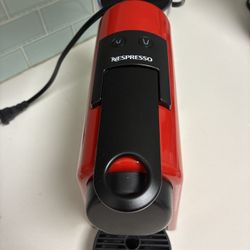 Red DeLonghi Nespresso Essenza Mini espresso machine. It's a compact and simple machine for making espresso. Includes a water reservoir and drip tray.