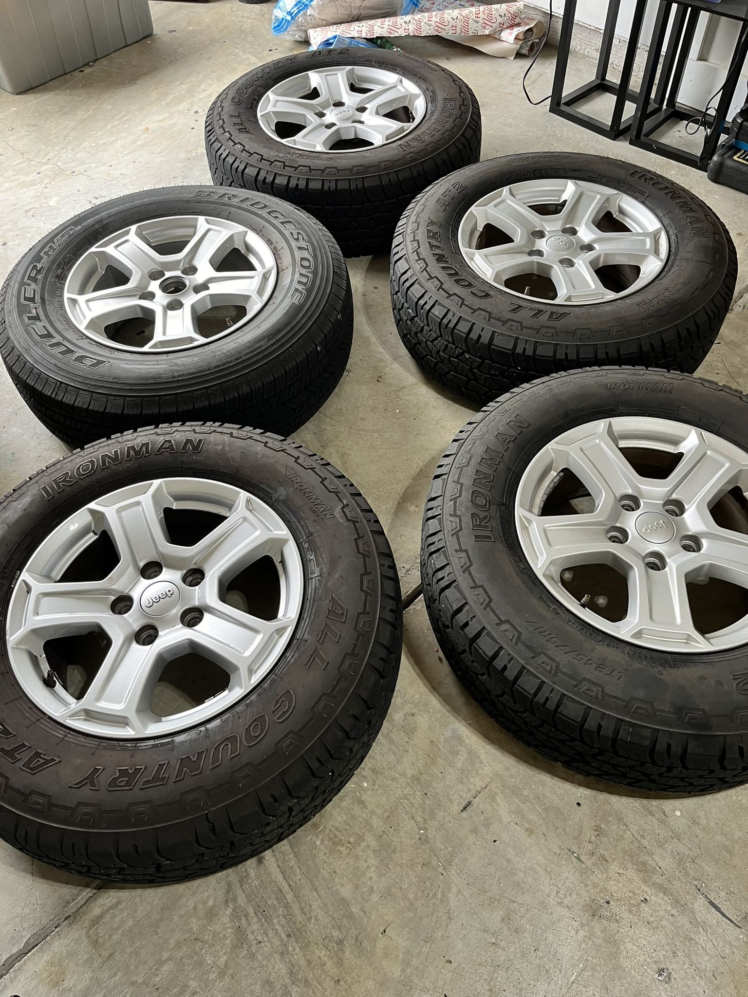 Set of 5 stock Jeep wheels with all-terrain tires.