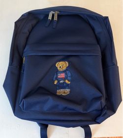 This navy blue Polo Ralph Lauren Polo Bear Backpack features an embroidered Polo Bear on the front pocket wearing a flag sweater