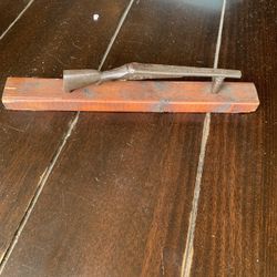 object in the image is a decorative item featuring a small, vintage metal rifle or shotgun