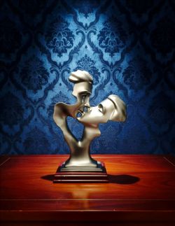abstract kissing couple face sculpture. It is an artistic home decor object crafted from durable resin with a painted metallic silver finish, measurin