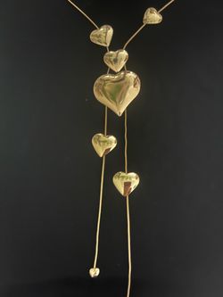 Elegant gold-toned necklace with multiple polished heart pendants. This piece has a lariat-style drop design featuring six hearts of varying sizes. Th