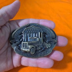 Vintage brass-toned metal belt buckle features a raised relief design of a semi-truck in front of a starred shield, flanked by two eagles. The bottom 