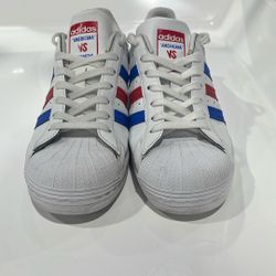 This is a pair of Adidas Americana vs. Superstar 'USA' sneakers in white with red and blue stripes. 