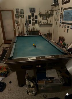 Pool table , balls, and rack with several pool sticks