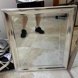 A rectangular wall mirror featuring a wide, polished silver frame.