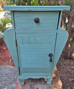 This item is a vintage Art Deco style reeded or pencil rattan bedside nightstand featuring a top drawer and a bottom storage cabinet painted in a dist