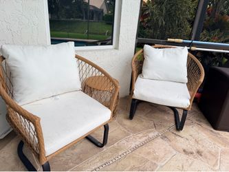 Woven wicker patio set includes two chairs and one round side table. Chairs have black metal sled bases and come with white seat and back cushions. Ma
