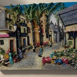 3D relief wall art that depicts a Mediterranean-style street or village scene. It is made from materials like hand-painted resin or layered paper cuto