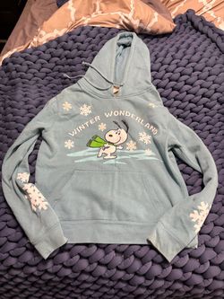 Cozy light blue women’s hoodie sweater featuring a festive Snoopy "Winter Wonderland" graphic.