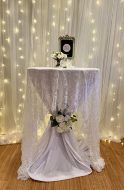 Elegant Wedding/Event Cocktail Table Setup  White table cover with delicate lace overlay Stylish floral arrangement with white roses & greenery 
