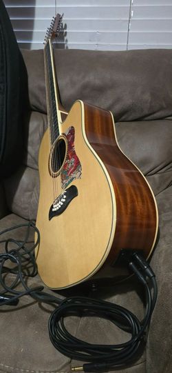 Oscar Smith 12-string acoustic-electric guitar has a natural finish spruce top with mahogany back and sides. This dreadnought cutaway model includes a