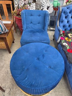 High-backed armchair upholstered in blue velvet with stud detailing, and a matching round ottoman.