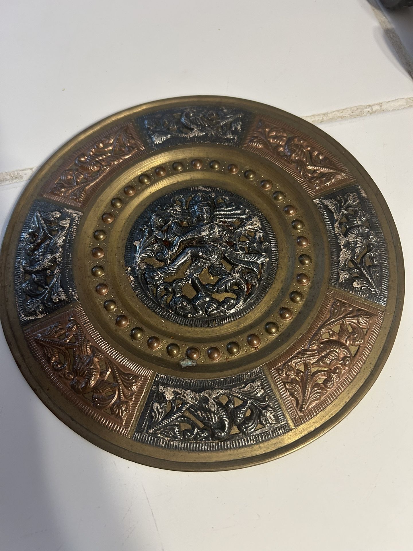 This is a vintage Indian mixed-metal decorative plate or charger, featuring brass, silver, and copper elements. The central figure is believed to be