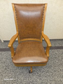 antique  style brown leather office chair with a wood frame and nailhead trim whith wheels 