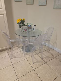 Dining table with 4 plastic chairs; the table features an aluminum base and a glass top.