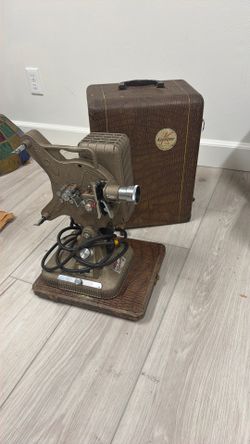 vintage film projector setup. The crocodile-pattern carrying case and metal body suggest a 1940s–1950s Keystone 8mm or 16mm movie projector made by Ke