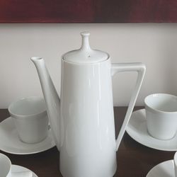 A white porcelain coffee pot with nine cups and saucers, likely Harmony House Moonglow.