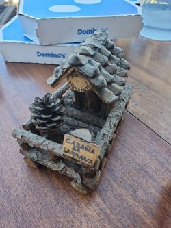 miniature cabin figurine is crafted from rustic natural materials like tree bark and pinecones.