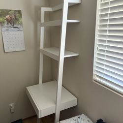 Crate and barrel desk that leans up against the wall with shelves