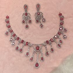 Red Statement American Diamond Necklace Set consists of a silver-plated necklace and matching earrings featuring red cubic zirconia stones. 