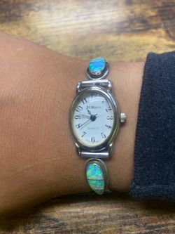Vintage St. Marin quartz watch with iridescent opal-style accents and silver-tone stretch band. Features blue/green flashes in the inlays and an oval 