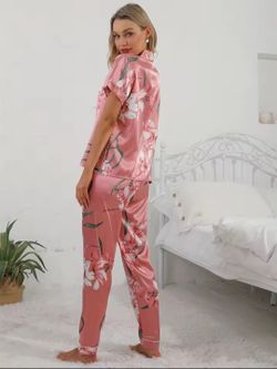 This pink floral satin pajama set features a short-sleeve button-down top with a lapel collar and matching long pants.