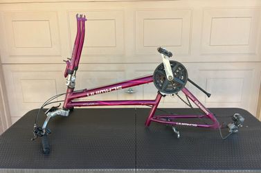 Disassembled purple Schwinn Third Avenue hybrid/comfort bicycle frame featuring an SR Suntour front suspension fork, crankset, and rear derailleur.