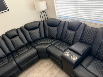 Modern black sectional sofa. It has a leather-like material with diamond stitching. Sofa has multiple reclining seats and a center console with two cu