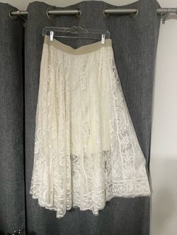 Elegant cream lace maxi skirt with an intricate floral and paisley pattern. This garment has a tan elastic waistband and a full-length silhouette. The
